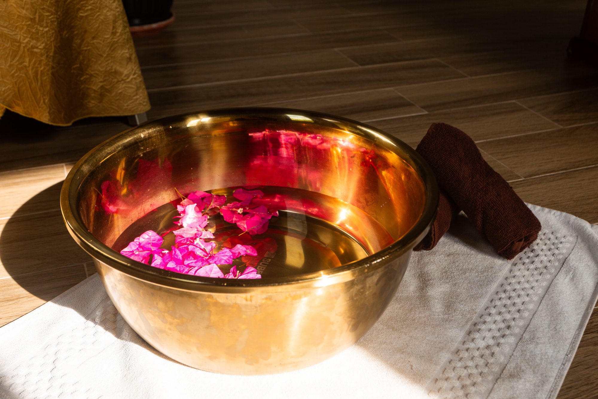 A brass bowl of warm water scattered with bougainvillea petals, set for the herbal foot soak