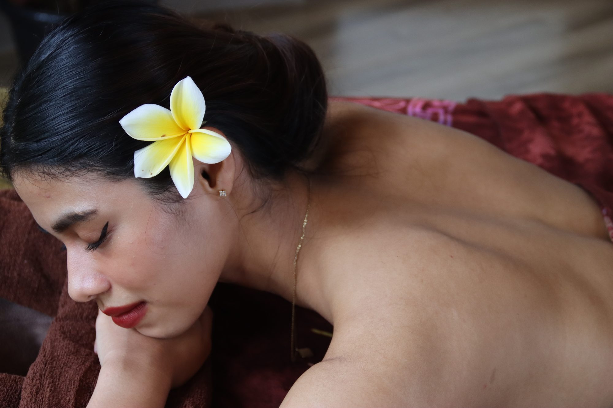 A guest resting on the treatment bed with a frangipani flower in her hair