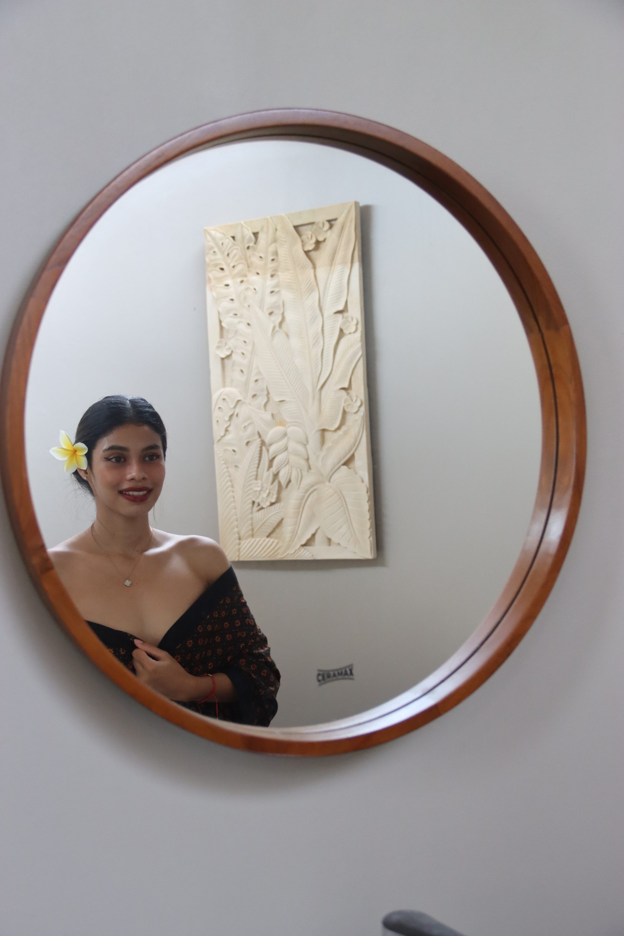 A guest reflected in a round timber mirror beside a carved Balinese relief panel