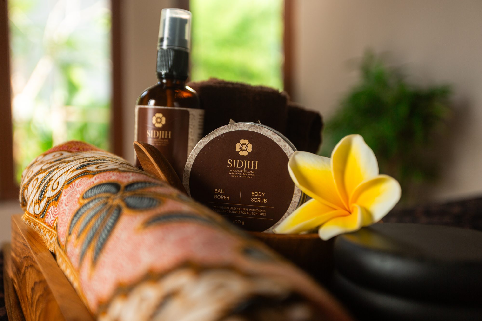 Sidjih Bali Boreh body scrub and massage oil resting on a carved wooden tray with frangipani