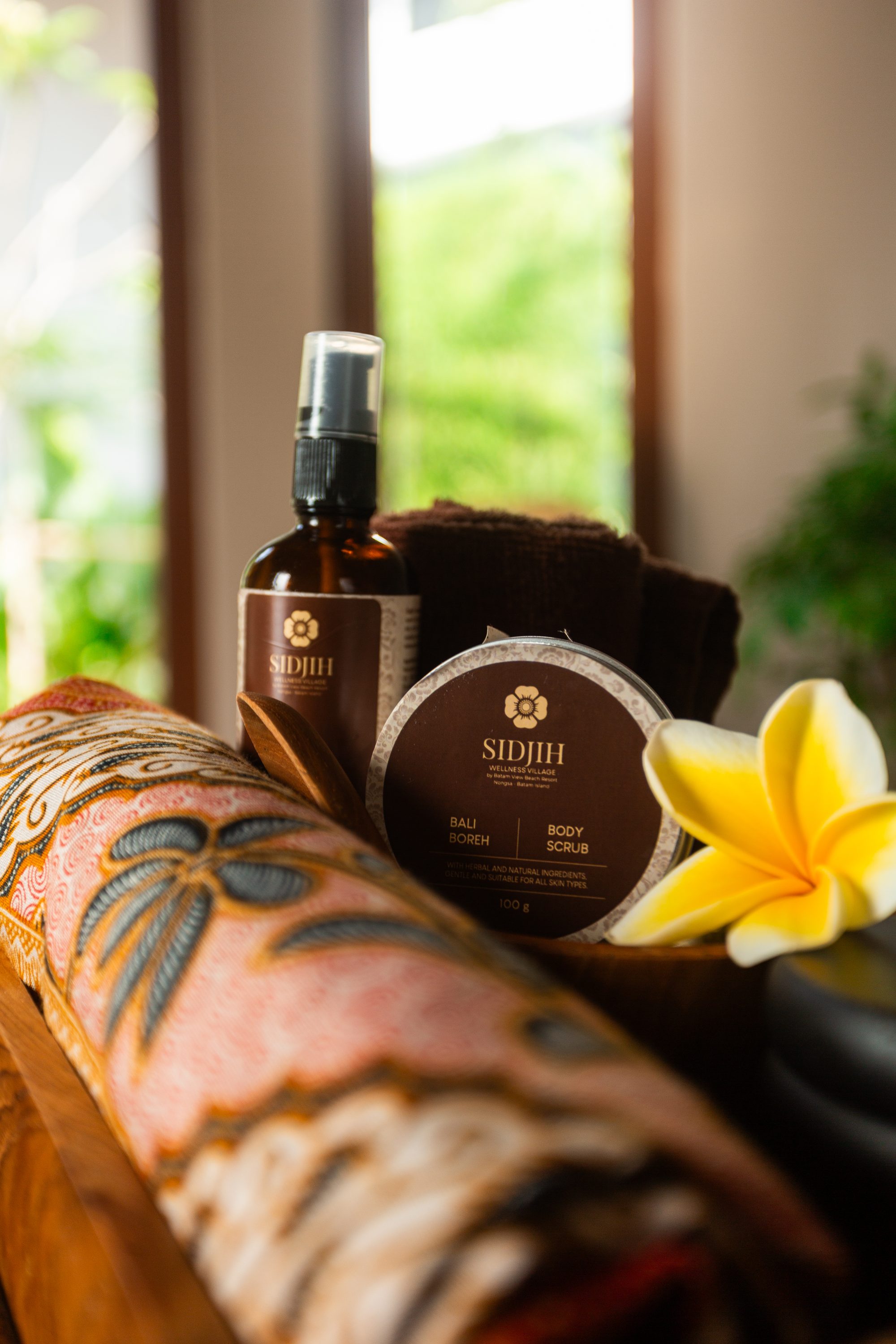 Sidjih body scrub and oil arranged with rolled towels and batik textile