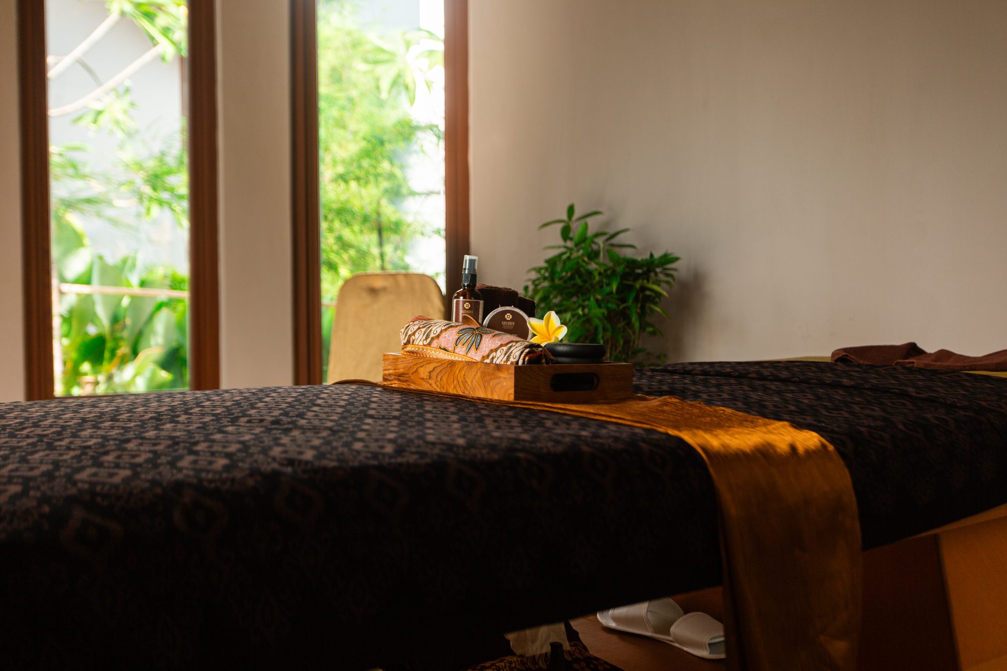 A treatment bed set with a therapist's tray of oils, stones and frangipani